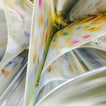A large webset offset printing press running a long roll off paper over its rollers at high speed.